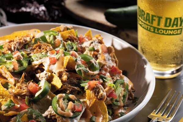 Nachos with toppings and a beer glass labeled "Draft Day Sports Lounge" on a table. - Grand Island Casino Resort (Grand Island)