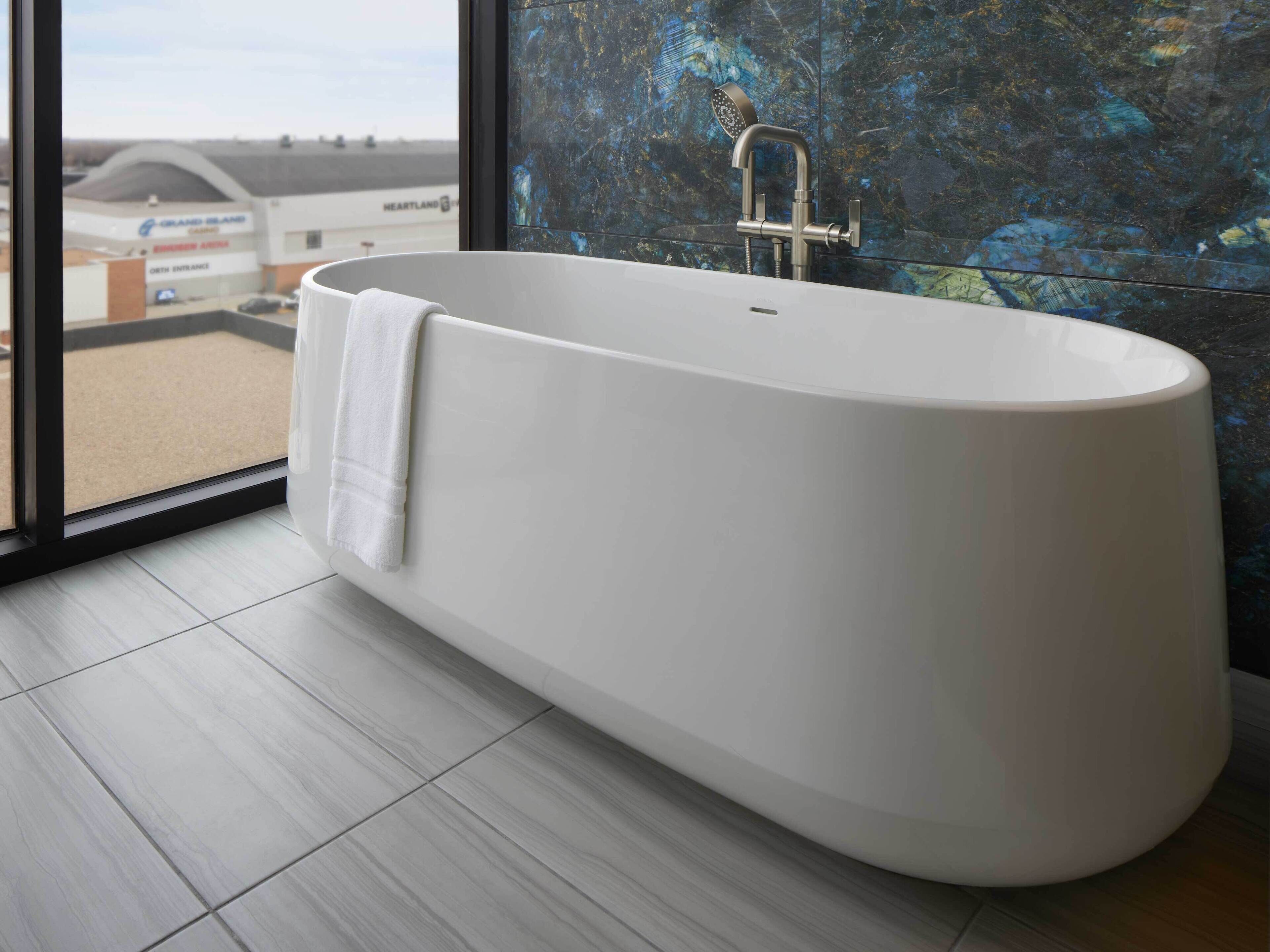 Un baño moderno con una bañera independiente, cabina de ducha con mampara de vidrio y vistas a un edificio comercial.