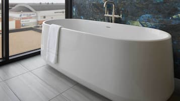 Un baño moderno con una bañera independiente, cabina de ducha con mampara de vidrio y vistas a un edificio comercial.