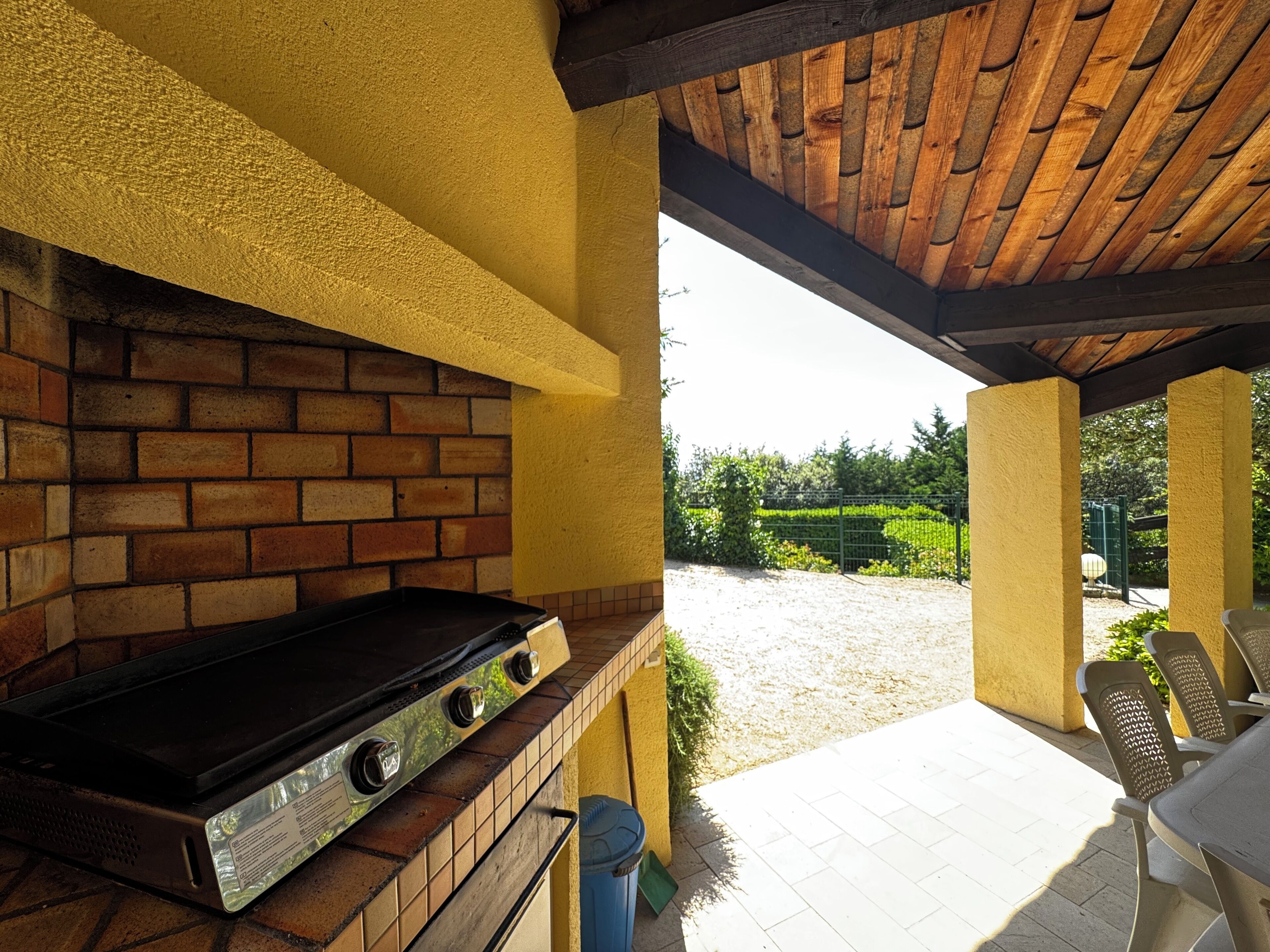 Une terrasse extérieure avec un mur en briques, un barbecue et une vue sur un jardin.