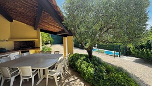An outdoor patio with a table and chairs, a brick fireplace, and a view of a swimming pool. - Le SIG - Swimming pool - 6 rooms (Piolenc)