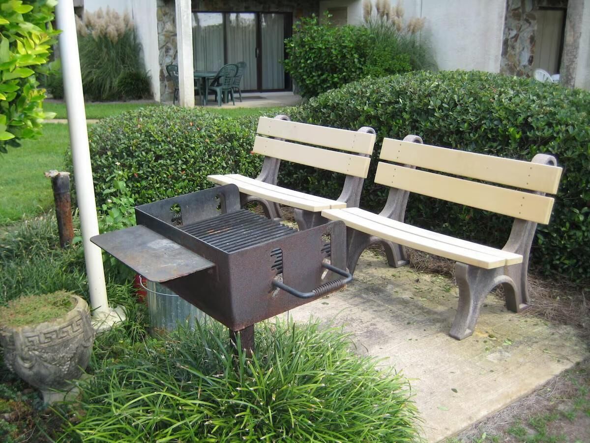 A barbecue grill and two wooden benches in a garden area.