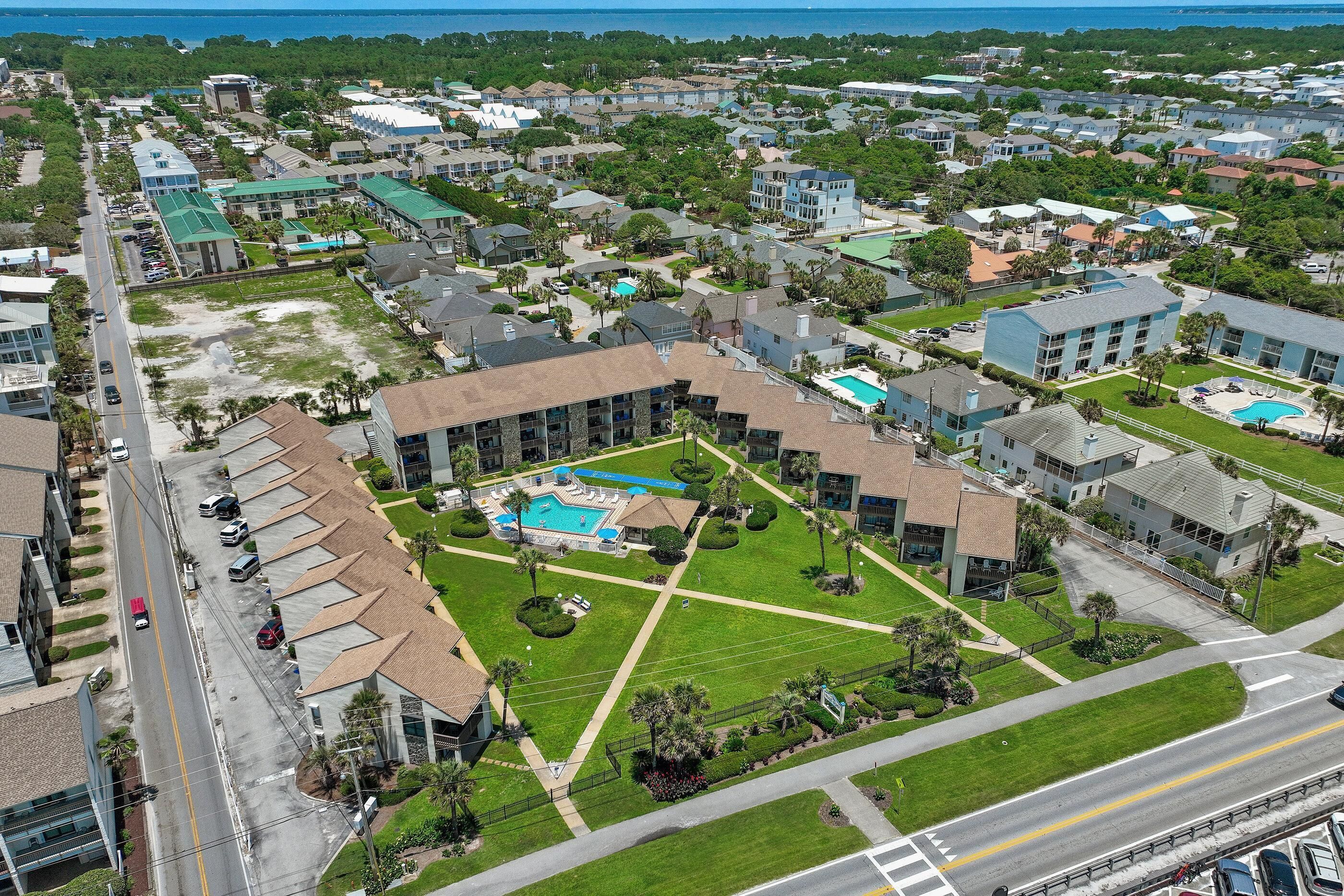 An aerial view of a residential area with a central courtyard featuring a swimming pool, surrounded by houses and greenery.