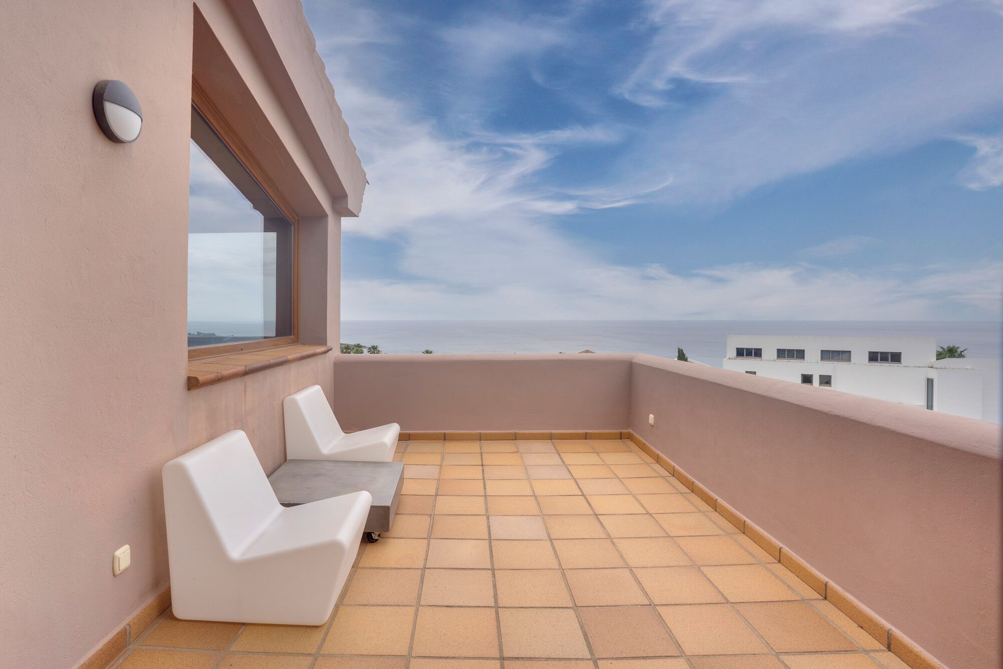 En balkon med to hvide stole og havudsigt under en klar himmel.