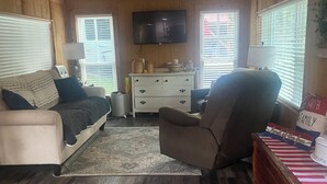 Una habitación acogedora con sofá, sillón, suelo de madera y televisión montada en la pared.