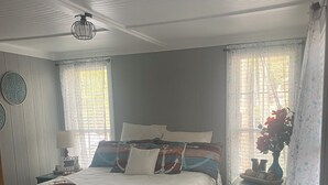 Un dormitorio con una cama grande, una mesita de noche, una lámpara y una ventana con cortinas.