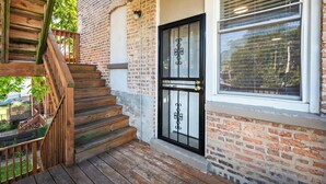 Una escalera de madera que lleva a un edificio de ladrillo con una puerta negra y una ventana con persianas.