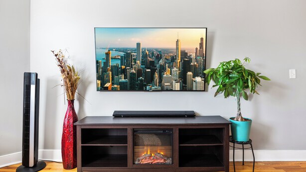Un salón con un televisor de pantalla plana montado en la pared, un mueble de centro de entretenimiento de madera oscura, un jarrón rojo con plantas secas y una planta en maceta verde.