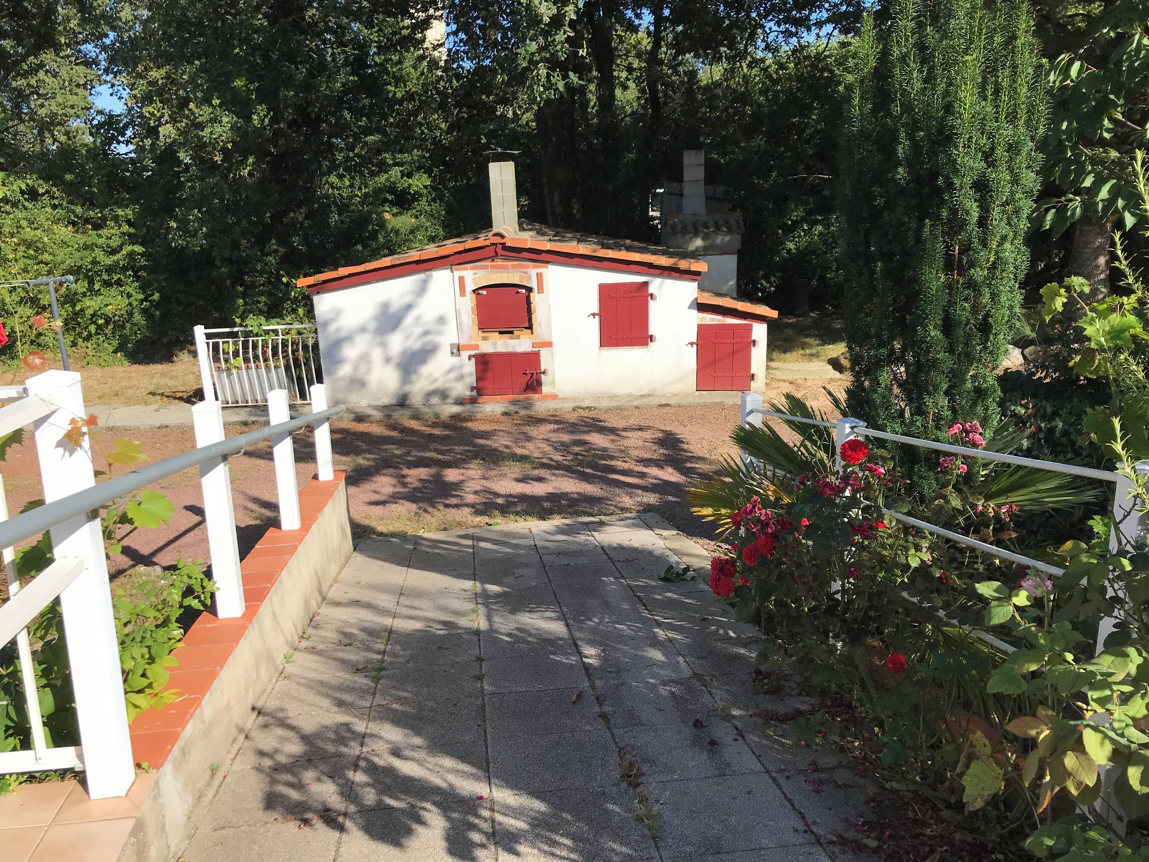 A pathway leading to a small building with a red roof and white walls, surrounded by greenery and flowers.