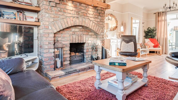 Una sala de estar acogedora con chimenea de ladrillo, un sofá cómodo, una mesa de centro de madera con libros y una alfombra roja.