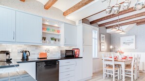 Una cocina moderna con armarios blancos, un lavavajillas negro y una zona de comedor con mesa y sillas blancas.