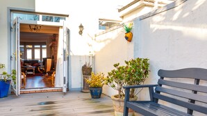 Un umbral abierto que da a una habitación con un sofá, una mesa, un banco y plantas en macetas sobre una terraza de madera.