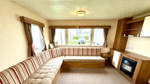 Ein gemütlicher Wohnbereich mit einer gebogenen Couch, einem Kamin und Blick ins Freie.