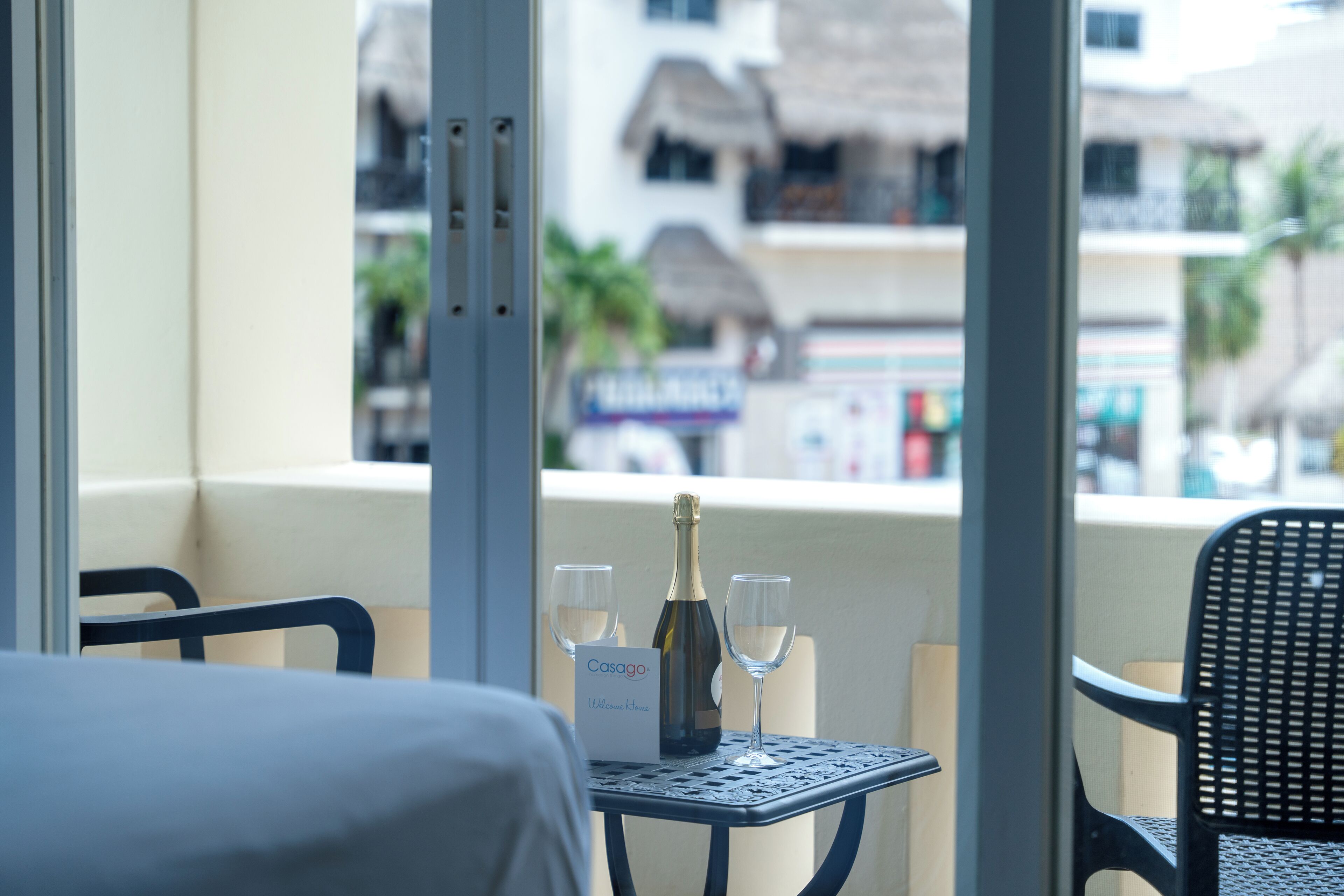 A balcony with a table set for two, featuring a bottle of champagne and two glasses, and a sign that reads "Casago Welcome".