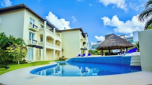Ein Resort mit Schwimmbad, einem Häuschen mit Strohdach und einem mehrstöckigen Gebäude mit Balkonen.