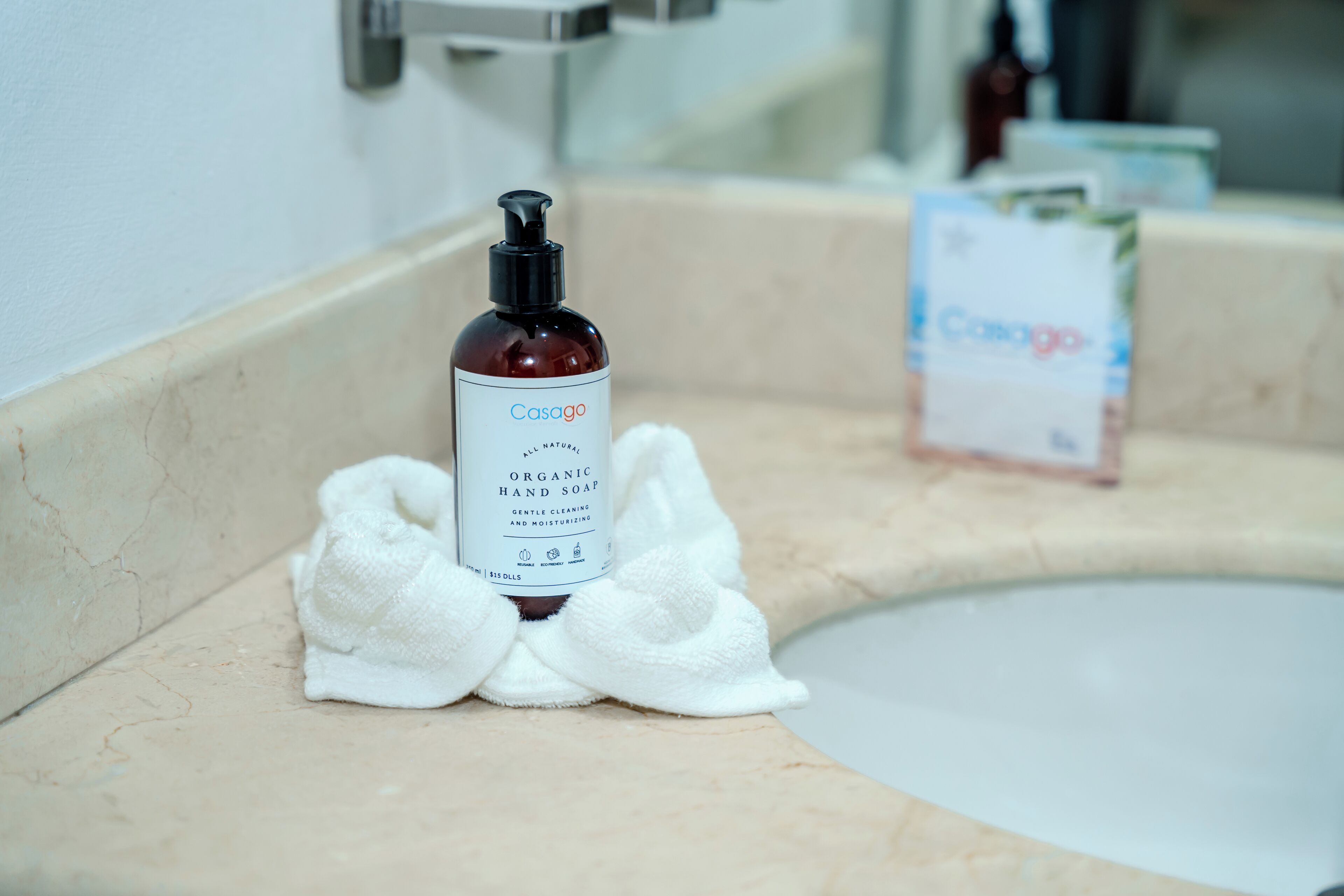 A bathroom sink with a bottle of Casogo Organic Hand Soap and a white towel.