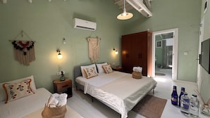 Une chambre avec deux lits, une armoire, une décoration murale en macramé, un climatiseur fixé au mur et une table de chevet avec une lampe.