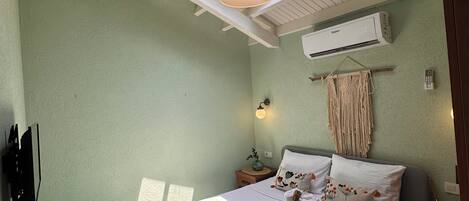 A bedroom with a bed, a bedside table, a wall-mounted air conditioner, a ceiling fan, and skylights.