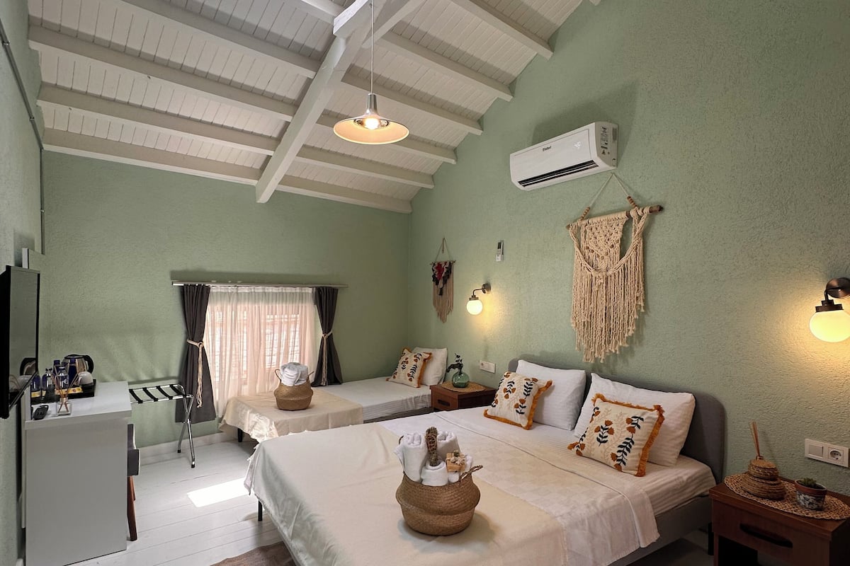 A hotel room with two beds, a desk, a small kitchenette, and a large window.