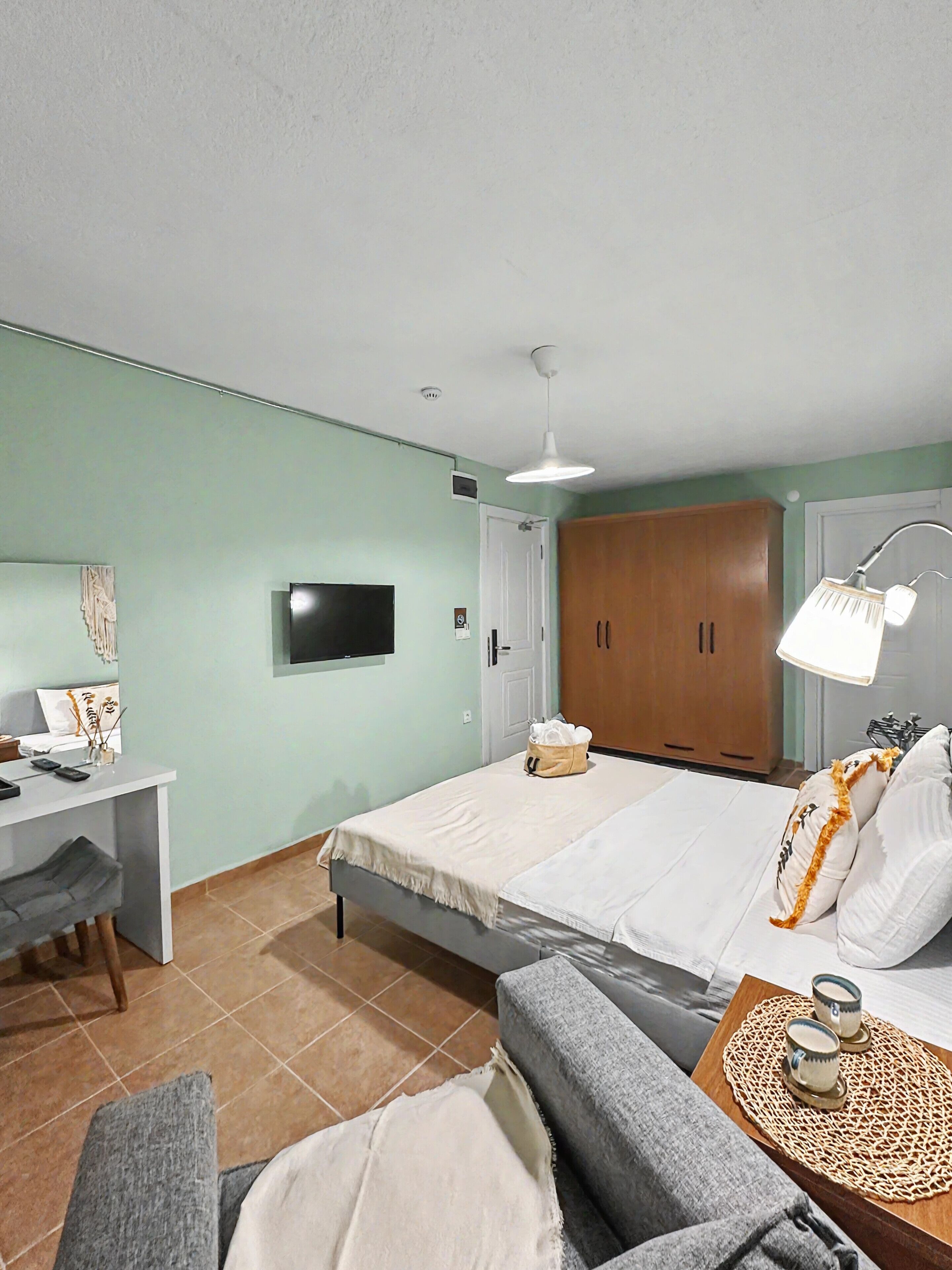 A hotel room with a bed, a desk, a television, a wardrobe, and a bedside table with a lamp.