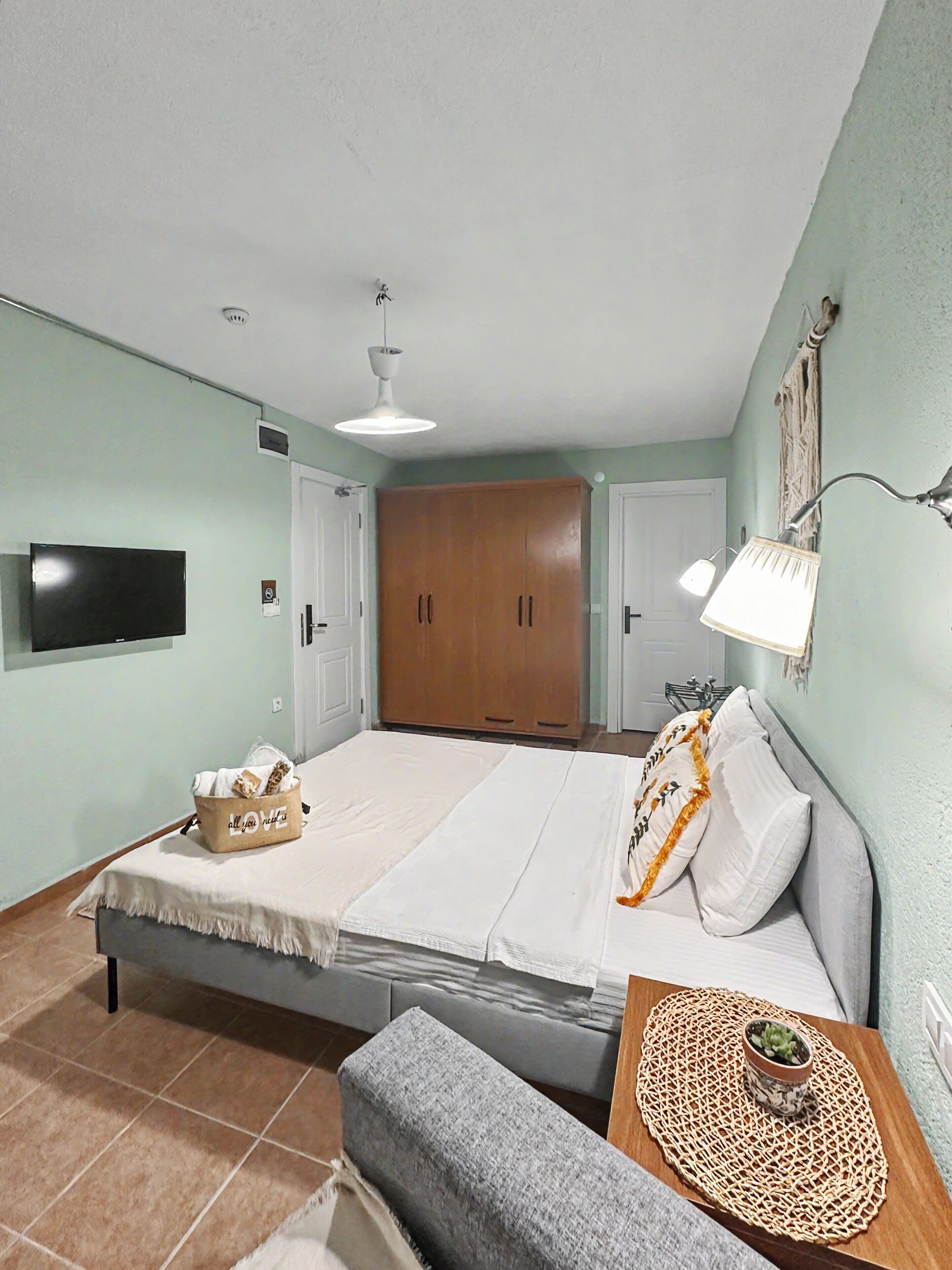 Un dormitorio con cama, televisor, armario y mesita de noche con lámpara.