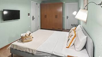 Un dormitorio con cama, televisor, armario y mesita de noche con lámpara.