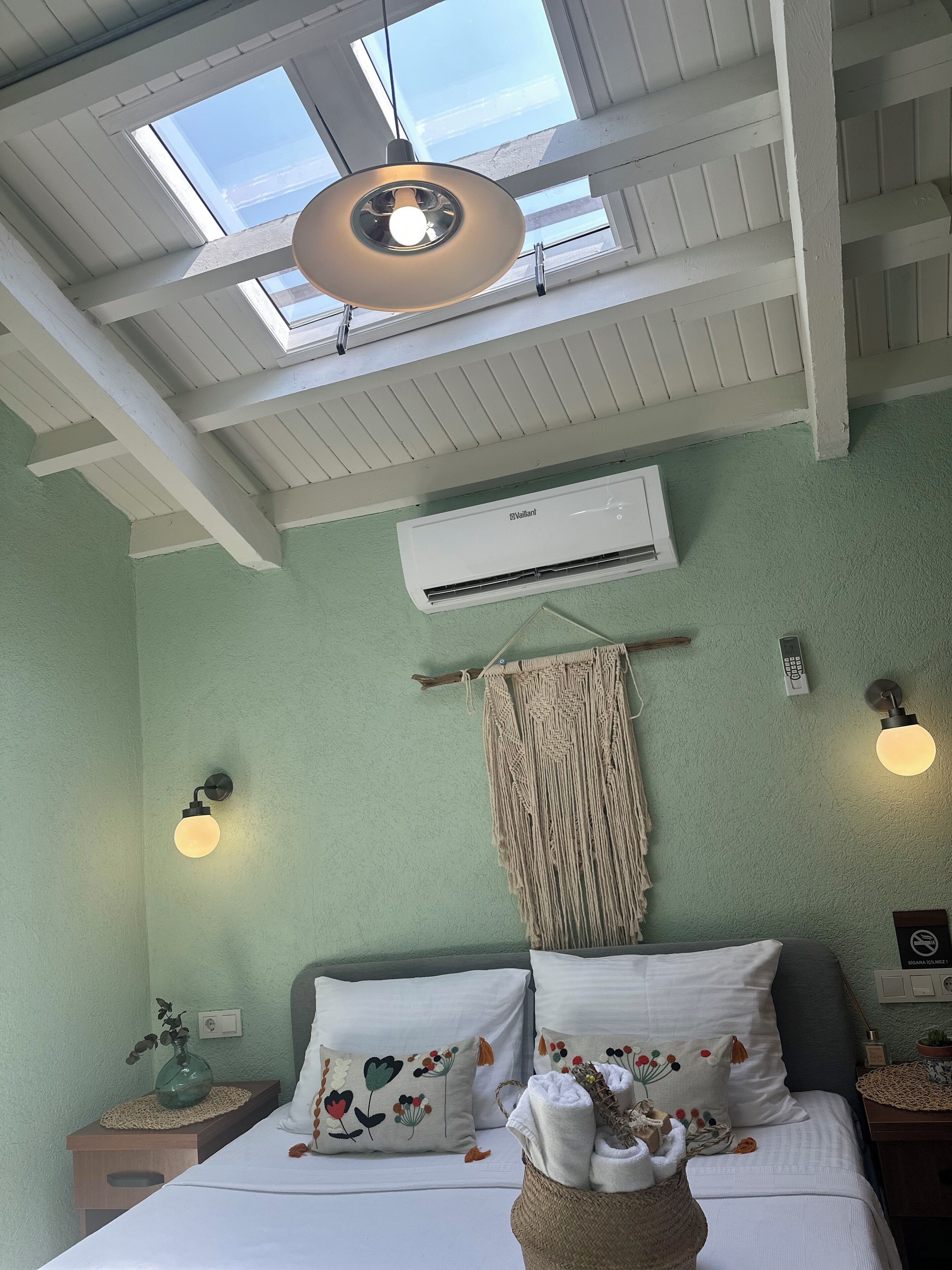 Ett rum med en säng, en väggmonterad luftkonditioneringsanläggning, en takfläkt och ett takfönster.