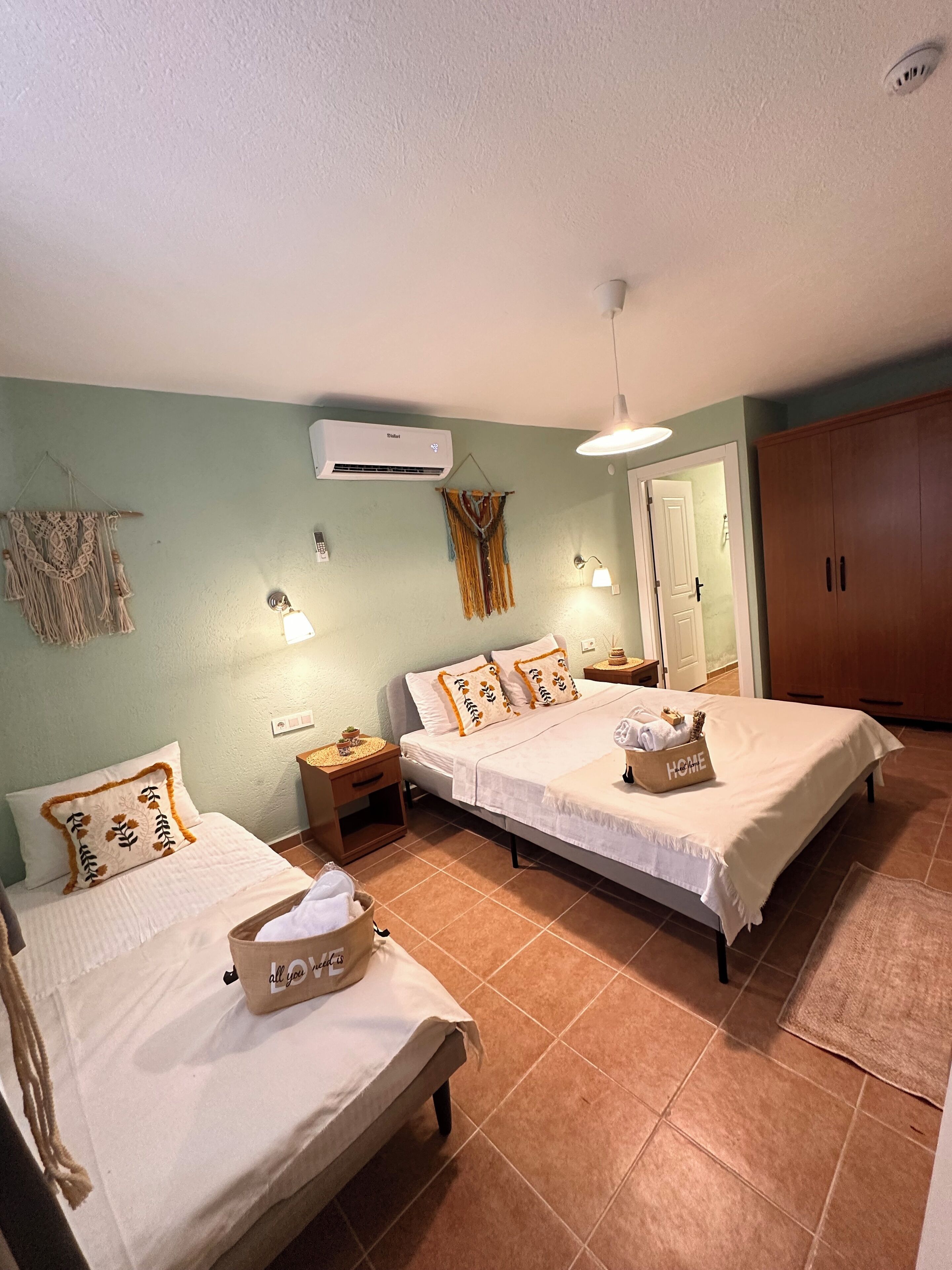 Un dormitorio con dos camas, un armario, aire acondicionado y una mesita de noche con lámpara.