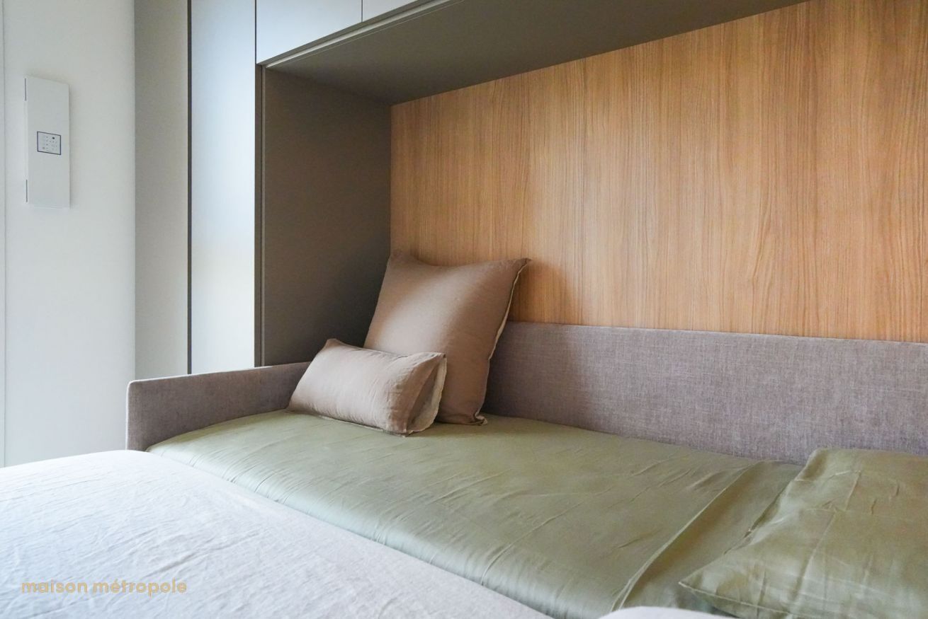 Ein modernes Hotelzimmer mit einem Bett, einem Holz-Kopfteil und einer grauen Sitzbank.