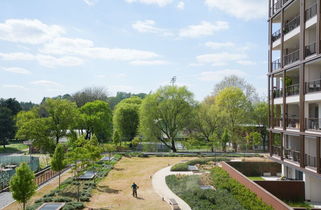 A modern apartment building with a landscaped courtyard featuring trees, a pathway, and a small pond.
