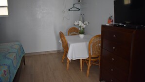 Ein Zimmer mit einem Bett, einem Esstisch mit Stühlen, einem Schrank, einem Fernseher und einer Wandklimaanlage.