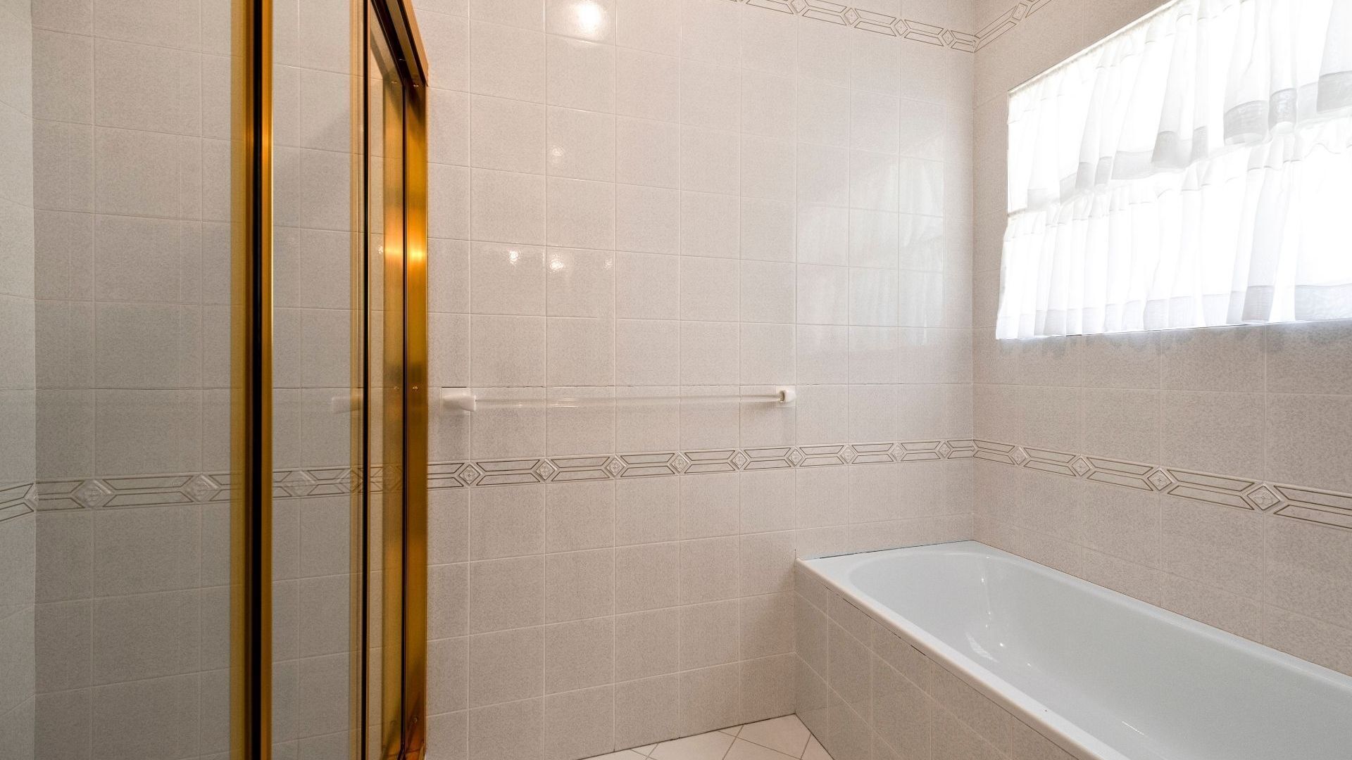 Une salle de bain équipée d’un espace douche, d’une baignoire et d’une fenêtre ornée de rideaux légers.
