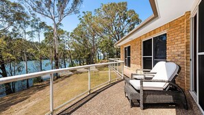 A balcony with wicker furniture, a view of trees, and a body of water.
