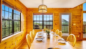 A wooden dining room with a large table set for six, large windows, and a view of a mountain. - 3 miles to Dollywood! Mountain views! Hot tub! Family fun! (Sevierville)