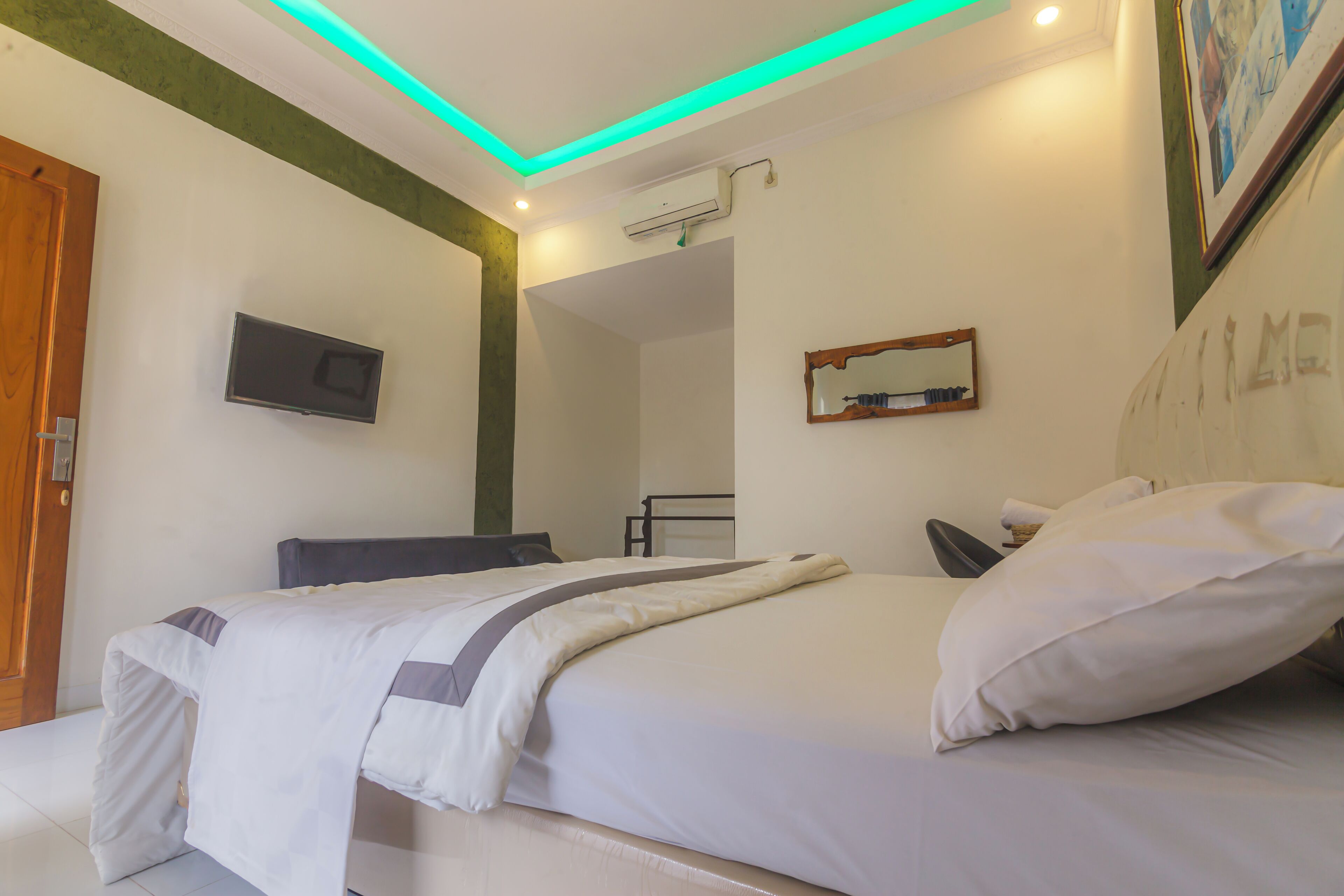 A neatly made bed with a white and gray bedspread, a bedside table with a lamp, and a wall-mounted TV.