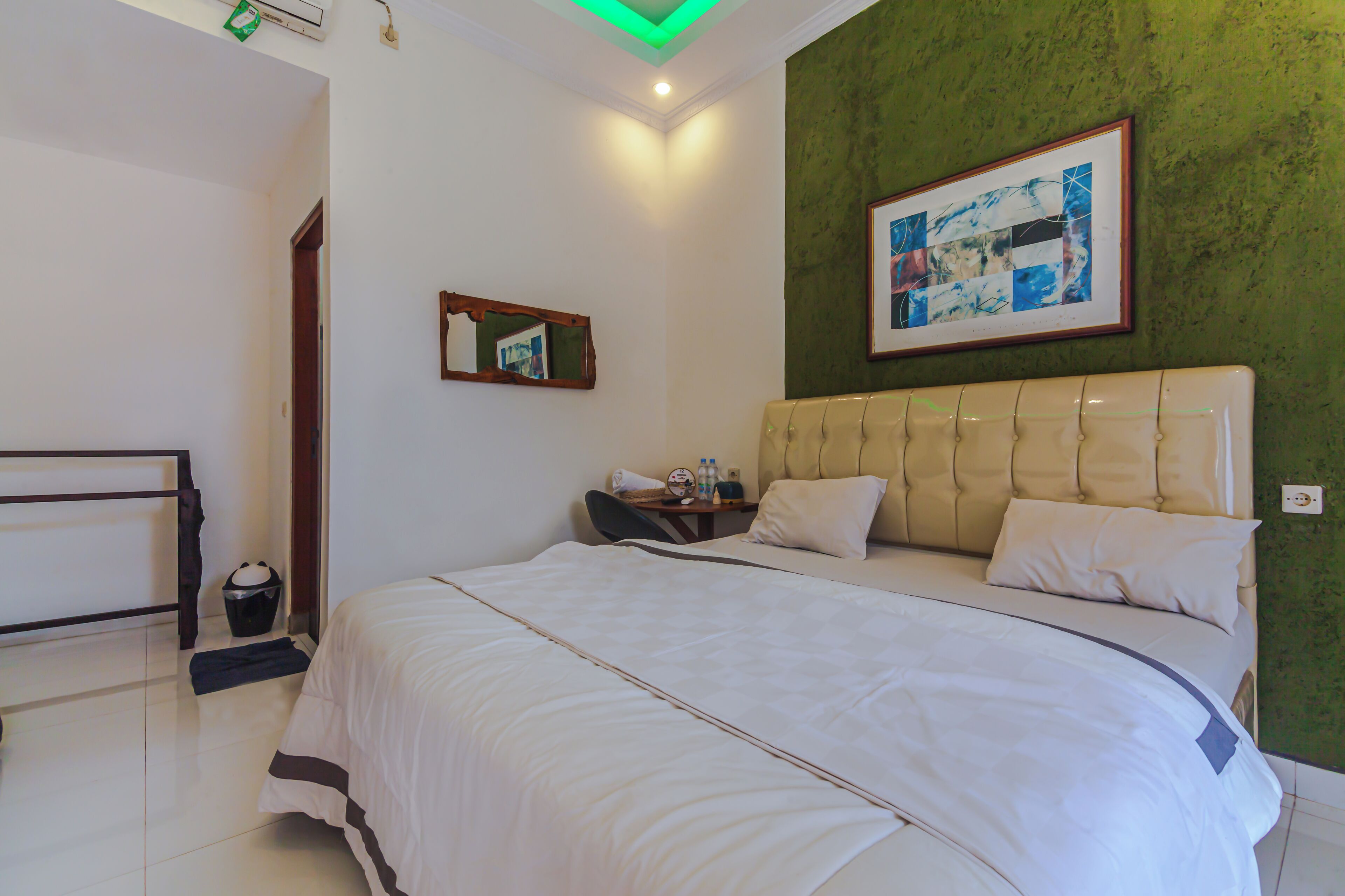 Habitación de hotel con una cama grande, una mesita de noche con lámpara, un cuadro enmarcado en la pared y una pared verde decorativa.
