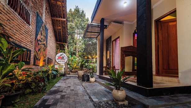 A courtyard with a paved walkway, potted plants, and a brick wall with a mural. - Morobudur Guesthouse (Borobudur)
