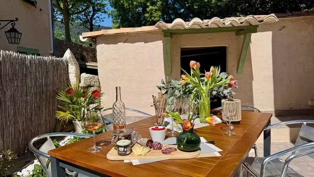 An outdoor dining area with a table set for two, featuring a variety of cheeses, cured meats, and a bottle of olive oil. - Under the eye of the bell tower (peymeinade)