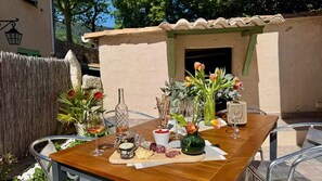 An outdoor dining area with a table set for two, featuring a variety of cheeses, cured meats, and a bottle of olive oil. - Under the eye of the bell tower (peymeinade)