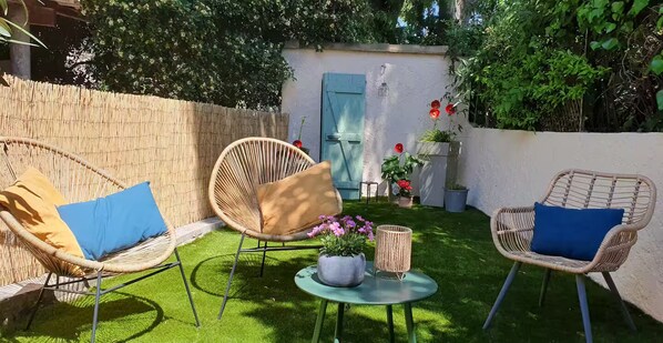 A patio area with wicker chairs, a small round table, and potted plants. - Under the eye of the bell tower (peymeinade)