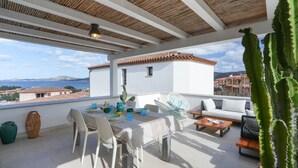 A terrace with a table set for dining, a sofa, and a cactus plant. - Cannigione | Dolce vita house terrazzo e vista (Cannigione)