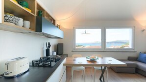 A compact kitchen with a gas stove, a toaster, and a dining area with a table and chairs. A window offers a view of the outdoors. - Cannigione | Dolce vita house terrazzo e vista (Cannigione)