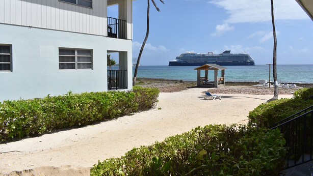 A beachfront property with a two-story building, a sandy beach, and a large cruise ship in the background. - Ocean View Studio - #7 (George Town)