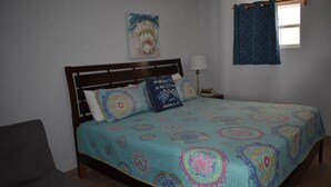 A bedroom with a bed, a nightstand, a lamp, a chair, and a window with curtains. - Ocean View Studio - #7 (George Town)