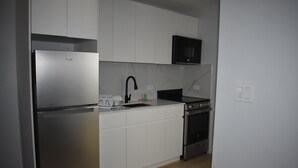 A modern kitchen with white cabinets, a stainless steel refrigerator, a microwave, and a stove. - Ocean View Studio - #7 (George Town)