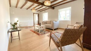 Un salón amplio con vigas de madera, un sofá blanco, un sillón de mimbre y una mesa de centro.