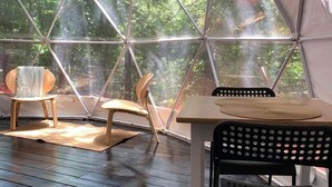 Eine geodätische Kuppelkonstruktion mit Holzboden, zwei Holzstühlen, einem Tisch mit gewebter Tischmatte und einem schwarzen, gelochten Stuhl.