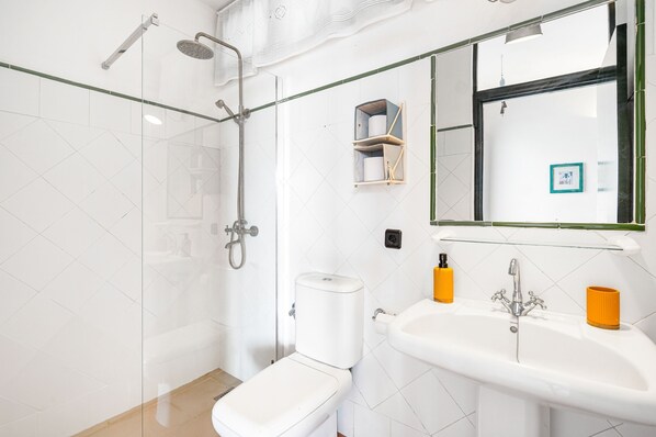 A modern bathroom with a glass shower enclosure, a toilet, a sink with two orange soap dispensers, and a mirror with a picture frame.