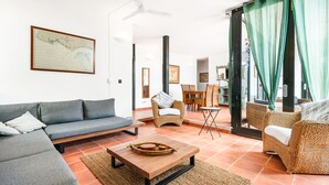 A modern living room with a grey sofa, wicker chairs, a wooden coffee table, and a dining area with a table and chairs.