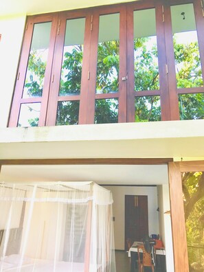 A room with a bed under a mosquito net, a wooden door, and a view of trees outside. - Relax in nature at ''Mount Heaven Araliya''Comfort, privacy, and calm await! (Hikkaduwa)